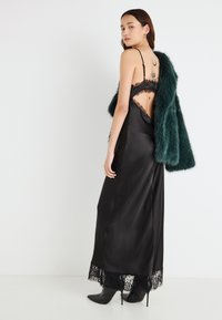 Μαύρο σατέν φόρεμα με δαντέλα στο τελείωμα, σχέδιο ανοιχτής πλάτης και ρυθμιζόμενους λεπτούς ιμάντες. Συνδυασμένο με παλτό από ψεύτικη γούνα σε σκούρο πράσινο χρώμα. Μαύρες γόβες στιλέτο.