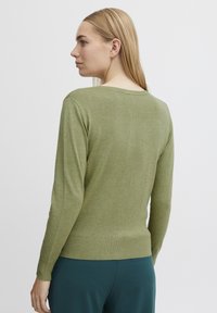 Pull vert à manches longues en matière douce, avec une coupe décontractée et un ourlet côtelé. Encolure arrondie, design simple sans motifs.