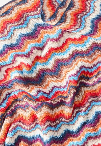 Tissu tricoté multicolore avec des rayures zigzag ondulées en orange, bleu, violet, rouge et blanc, montrant la texture et des plis pliés.