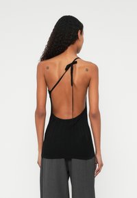 Svart strikket halterneck topp med åpen rygg, med en knytelukking i nakken og et teksturert mønster. Kombinert med grå vide bukser.