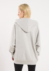 Grå oversized hettegenser med snorhette, lange ermer og ribbede mansjetter. Myk tekstur, løs passform og ingen synlige mønstre.