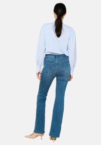 Camisa a rayas azul, de corte relajado y mangas largas, combinada con unos pantalones vaqueros de campana de talle medio. Presenta bolsillos traseros y un acabado suave.