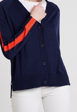 Cardigan navy con scollo a V, cinque bottoni e dettaglio a strisce arancioni sulle maniche. Texture morbida e orlo a coste, con spacco laterale.