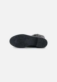 Semelle en caoutchouc noir avec des rainures texturées et un design de cheval. Le matériau supérieur présente une surface texturée et sombre pour plus de durabilité.