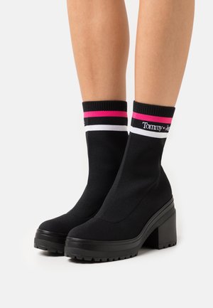 Bottines style chaussette noires avec une finition texturée, dotées d'un talon bloc haut et d'accents rayés colorés sur la bordure supérieure.