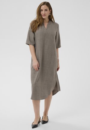 Woman with long hair wearing a gray midi dress with half sleeves and black slingback heels, standing against a plain background.