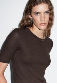 Hnědý pletený top s krátkým rukávem a kulatým výstřihem. Lehký a přiléhavý design, který zvýrazňuje tvar těla. Hladká textura.