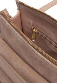 Interno di una borsa a tracolla in pelle marrone chiaro con una superficie liscia, dotato di una tasca con zip e hardware della cerniera in tonalità dorata. Scomparti per l'organizzazione.