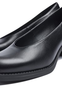 Zapatos negros de cuero sin cordones con textura suave, punta redondeada y tacón modesto, con costuras visibles y suela de goma duradera.