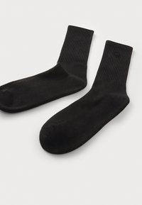 Calcetines de algodón negros con un puño acanalado, texture suave y puntera reforzada. Presentan un logo sutilmente grabado en el puño.