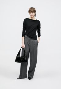 Μαύρο μακρυμάνικο τοπ, γκρι φαρδιά παντελόνια ψηλόμεσα, και μια μαύρη τσάντα από συνθετικό δέρμα, σε απλό λευκό φόντο.