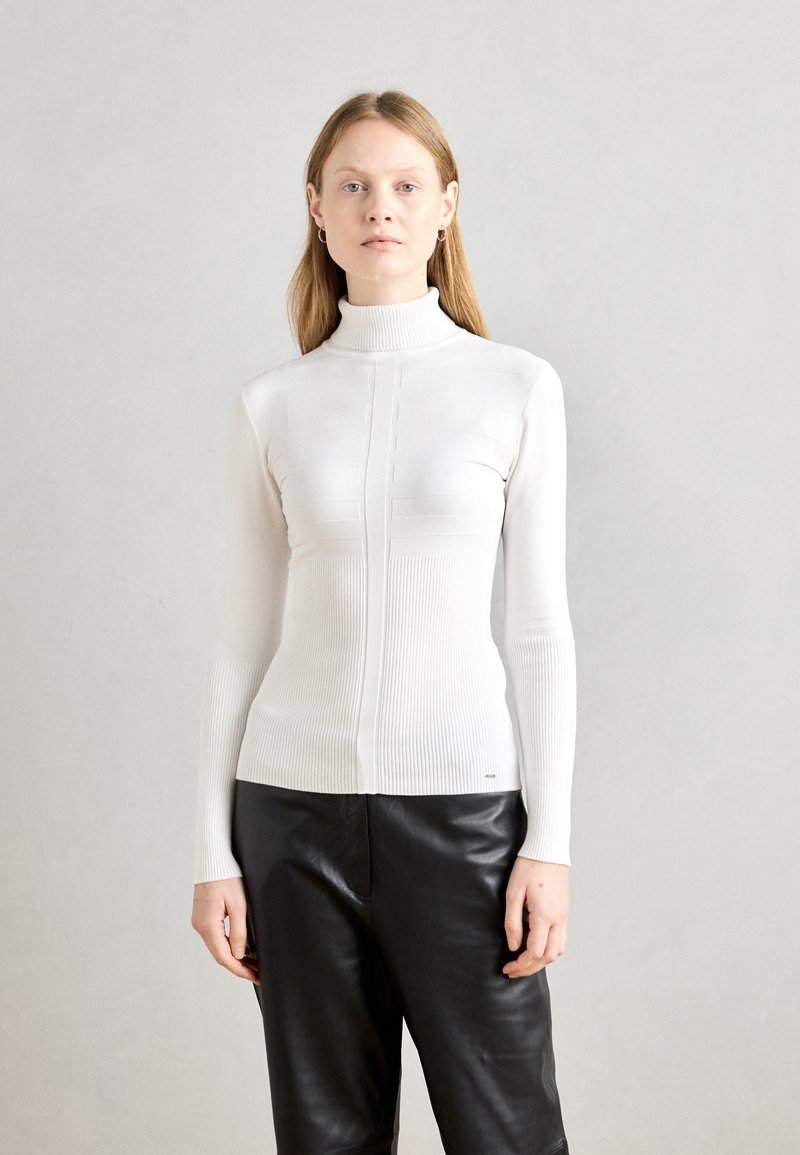 Weißer gerippter Rollkragenpullover mit taillierter Silhouette und vertikaler Bandelementierung, kombiniert mit schwarzen Lederhosen für den Kontrast.