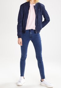 Marinblå bomberjacka, randig rosa och vit topp, slim fit blå jeans och vita sneakers. En enkel, figurnära design med slät finish.