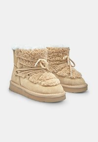 Béžové pletené členkové boty s fleecovým zvrškom, semišovou spodnou časťou a rebrovanou podrážkou. Obsahujú dekoratívne šnurovanie a jemný, textúrovaný povrch.