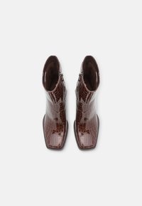 Bottines en cuir marron brillant avec un motif crocodile, bout carré et fermeture éclair sur le côté. Texture lisse et design épuré.