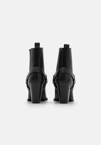 Botas de tobillo de cuero negro con un diseño elegante, tacones altos en bloque y un detalle de cinta lateral. Acabado suave y parte trasera sin costuras.