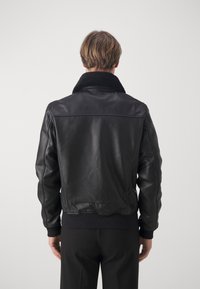 Svart läderjacka med shearlingkrage, ribbade ärmslut och en figursydd design. Slät yta med detaljerad sömnad på baksidan.