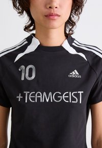 Black athletic shirt featuring a prominent white collar, three white stripes on the shoulders, and silver embroidered details, including "#10" and "+TEAMGEIST."