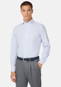 Camicia a righe in azzurro chiaro e bianco, maniche lunghe, colletto abbottonato, abbinata a una cintura intrecciata blu navy e pantaloni grigi plissettati.