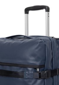 Marineblauer Reisetasche mit Rollen und einer strukturierten Stoffoberfläche, verstellbarem Teleskopgriff und einem schwarzen Sicherungsriemen mit Knebelverschluss.