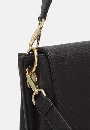 Czarny, teksturowany róg skórzanej torby z złotymi metalowymi klamrami i pierścieniami mocującymi regulowany pasek.