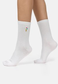 Calzini crew bianchi in cotone con bordi a coste e un cono gelato ricamato di colore azzurro chiaro, rosa e giallo sul lato. Tessuto morbido, design casual.
