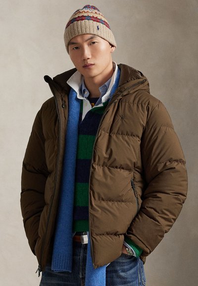 Brown puffer jacket with a hood, featuring quilted design. Worn over a blue and green striped sweater and a collared shirt. Knit patterned hat.