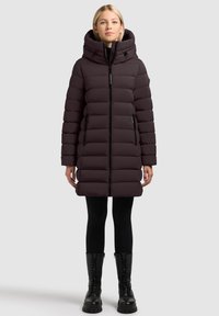 Kurtka puchowa w ciemnym fioletowym kolorze, z kapturem, z przednim zamkiem błyskawicznym, o fakturze prążkowanej, z dwoma bocznymi kieszeniami. Noszona na czarnych legginsach i wojskowych butach.