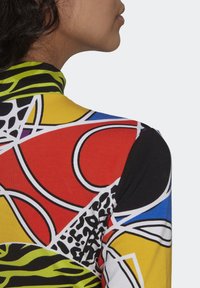 Färgglad långärmad topp med en blandning av djärva geometriska mönster i röd, gul, svart, grön och blå mot en vit bakgrund.