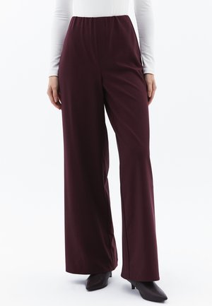 Bordeaux wijde broek met een hoge elastische tailleband, gemaakt van zachte, gladde stof, getoond naast een aansluitend wit langemouwtop en hoge hakken.