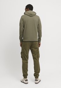 Olive green hoodie with a spacious hood and ribbed cuffs, paired with cargo pants featuring multiple pockets and elastic cuffs.