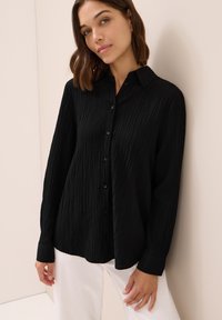 Camicia nera con bottoni, in tessuto testurizzato, maniche lunghe e colletto. Presenta una vestibilità relaxed e dettagli dei bottoni a vista.