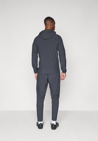 Donkergrijs sportief trainingspak met een capuchonjack en taps toelopende broek, gemaakt van lichtgewicht stof met elastische boorden.