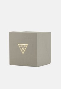 Cutie gri din carton cu o suprafață texturată, având un logo triunghiular auriu cu un semn de întrebare pe față. Design compact și unghiular.