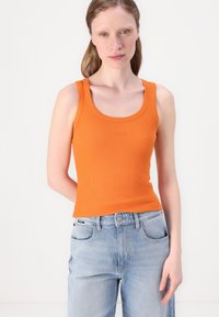 Oransje ribbet tanktop med rund hals. Kombinert med lyseblå høy midje jeans, med to frontlommer og logomerke.