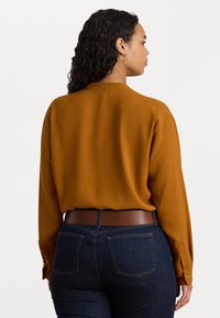 Κατακόκκινη μακρυμάνικη μπλούζα με πίσω γιακά και κουμπωτές μανσέτες, συνδυασμένη με σκούρα μπλε τζιν και καφέ ζώνη. Μαλακή υφή.