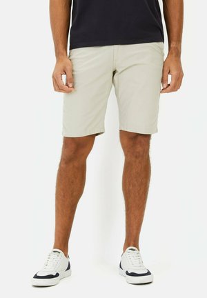 Beige shorts made of lightweight fabric, featuring a flat front, side pockets, and a straight cut. Paired with white sneakers.