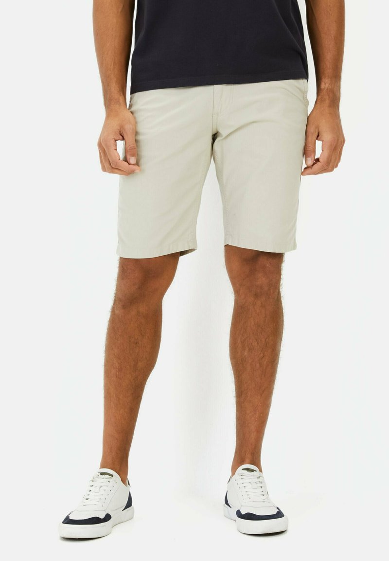 Beige shorts gemaakt van lichtgewicht stof, met een rechte voorkant, zijzakken en een rechte snit. Gecombineerd met witte sneakers.