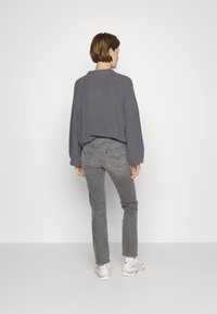 Maglione grigio lavorato a maglia con scollo rotondo, maniche lunghe e vestibilità morbida, abbinato a jeans grigi e sneakers di tonalità chiara.