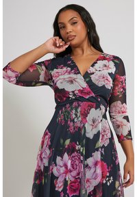 Navy sininen kukkakuosisessuuki, jossa on 3/4 läpikuultavat hihat, V-pääntie ja sekoitus pinkkejä ja valkoisia kukkia vihreillä yksityiskohdilla.