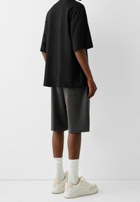 T-shirt noir à manches courtes, shorts gris, chaussettes blanches et baskets beiges. Tissu lisse avec une coupe décontractée. Design minimaliste, sans motifs.