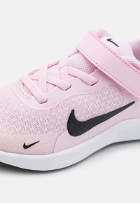Zapatilla deportiva Nike de color rosa con parte superior de malla, logotipo Swoosh negro, superficie texturizada, cordones y una correa de velcro. Suela blanca.
