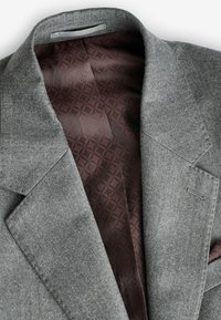 Grijze wollen blazer met een opstaande revers. De binnenkant heeft een donkerburgundy voering met een geometrisch patroon. Schoon, op maat gemaakte ontwerpdetails zichtbaar.