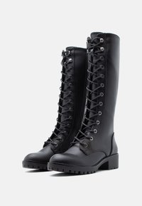 Bottes noires en cuir montant jusqu'aux genoux avec un laçage avant, bout rond, surface texturée, œillets en métal et un talon carré solide.