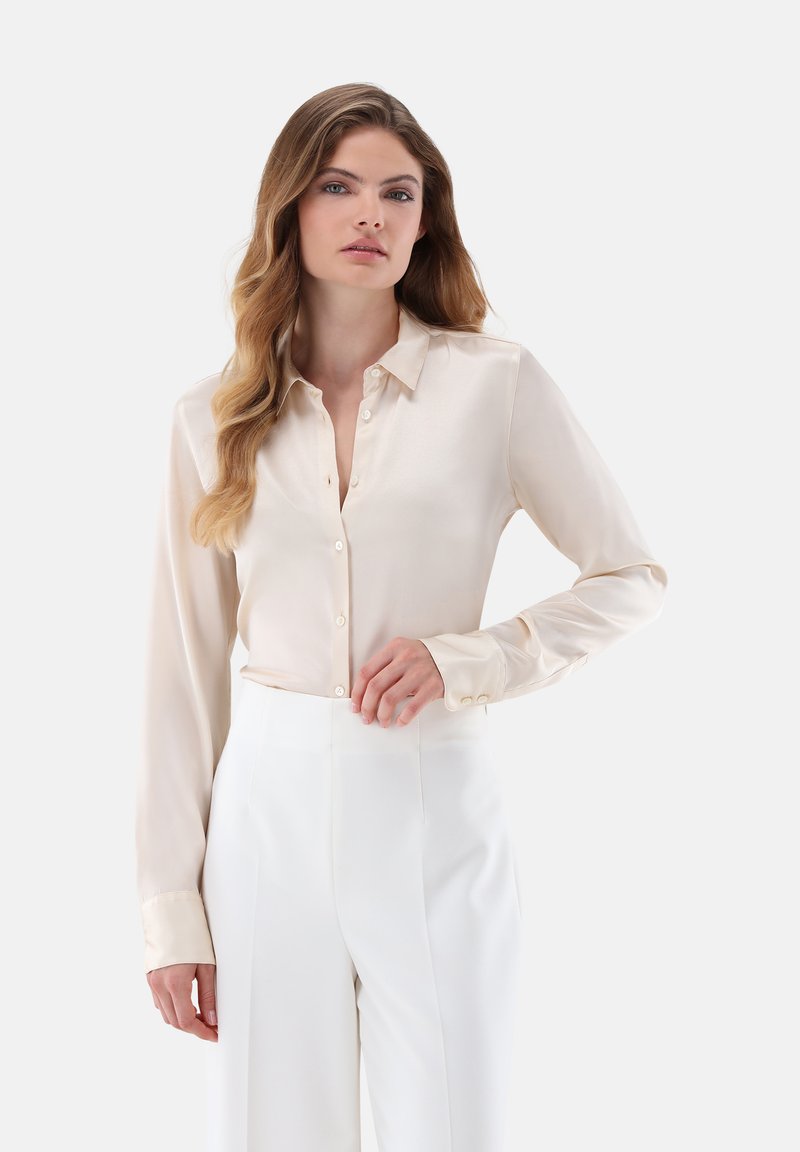 Cream button-up blouse with long sleeves, subtle sheen, and a classic collar, paired with high-waisted white trousers.