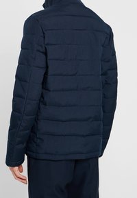 Marinblå puffy-jacka med quiltad finish och hög krage. Har en rak passform, texturerad tyg och sydd paneldesign.