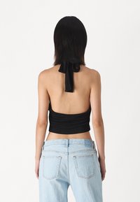 Svart halterneck-topp med samlet stoff, åpen ryggdetalj og en sløyfe rundt halsen, kombinert med lyseblå denimjeans.