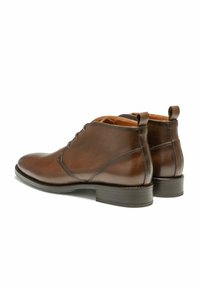 Bottes de cheville en cuir marron avec une finition lisse, bout rond, deux petites languettes de traction et coutures surélevées ; talon empilé pour la stabilité.