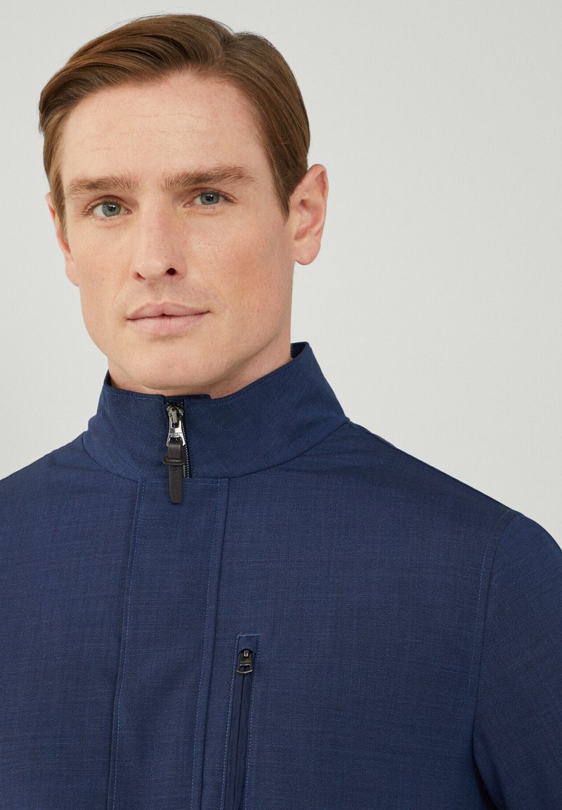 Veste zippée bleu marine avec un col haut, tissu texturé, poche zippée à l'avant et détails de couture subtils.