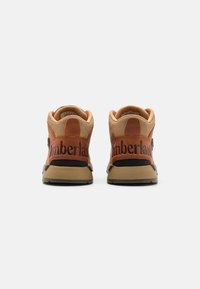 Zapatillas altas de cuero marrón y sintético color beige con detalles en negro. Presentan el logo "Timberland" en el talón y una suela de goma texturizada.